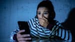 Frightened teenager or young woman using smart mobile cell phone as internet cyberbullying by message stalked abused victim.